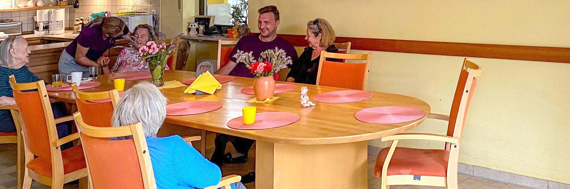 Seniorengruppe mit Pflegekraft in einer Wohngemeinschaft am Essenstisch Seniorengruppe mit Pflegekraft in einer Wohngemeinschaft am Essenstisch